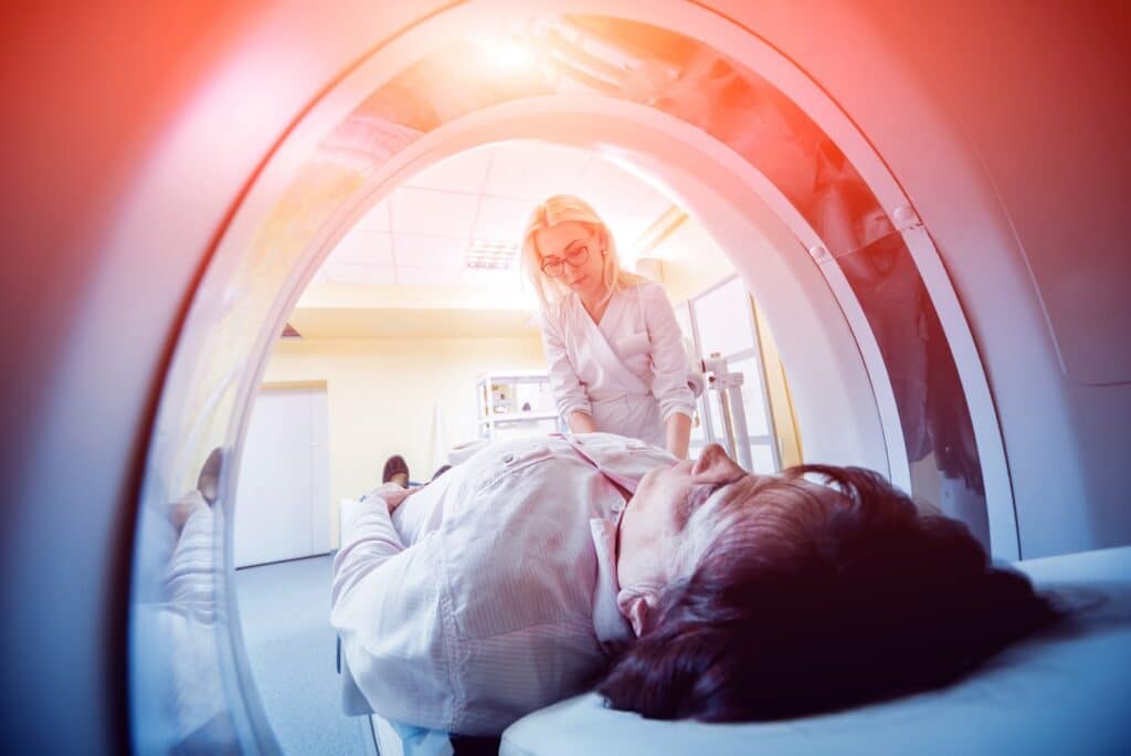 A woman undergoing diagnostic imaging as a female medical technician adjusts the bed.